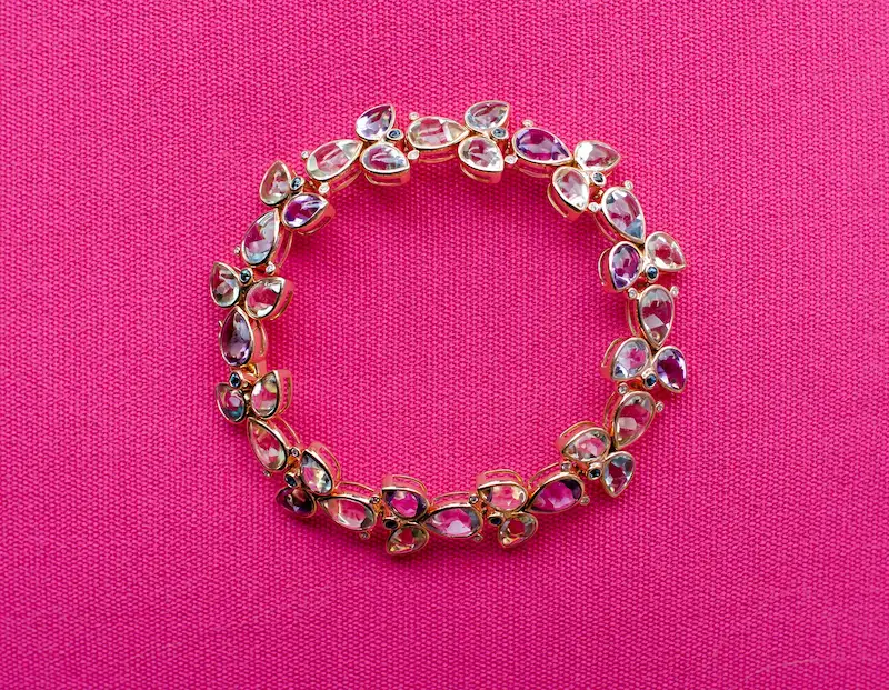 Armband mit farbigen Steinen auf pinkfarbenem Hintergrund.