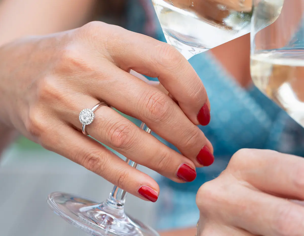 Nahaufnahme einer Hand mit Ring bei einem Glas Wein.